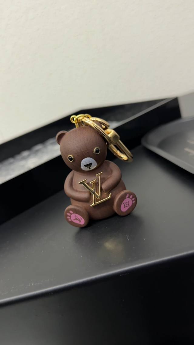 M01360 Lv Teddy Bear 包饰与钥匙扣 Lv Teddy Bear 包饰与钥匙扣为路易威登动物家族再添憨厚一员。黄檀木塑造怀抱 Lv 字母的小熊